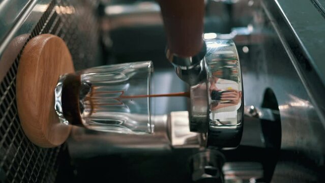 Vertical video: Pouring coffee stream from professional machine in cup. Barista man making espresso shot by bottomless, using filter holder. Flowing fresh ground coffee. Drinking roasted black coffee.