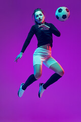 Plakat In action. One sportive girl, female soccer player training with football ball isolated on purple studio background in neon light. Sport, action, motion, fitness