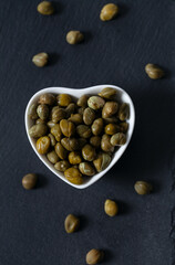 Canned cappers on black stone surface. Gourmet food.