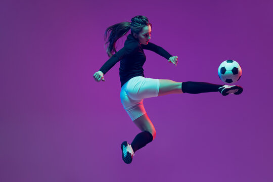 In action. One sportive girl, female soccer player training with football ball isolated on purple studio background in neon light. Sport, action, motion, fitness - Powered by Adobe