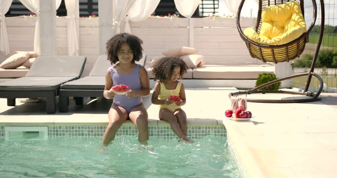 Two little girls sitting at poolside and eating watermelon