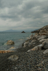 rocks on the pebbles beach across the horizon across dramatic sky and mountains. Summer nature background