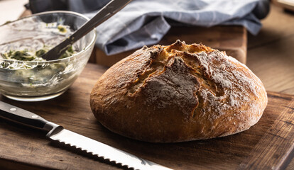 Crusty bread loaf next to a knife and butter mixed with herbs in a bowl