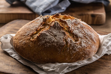 Homemade baked crusty bread places on a linen towel and wooden cutting board