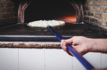 The pizza chef bakes a white pizza, only mozzarella, in the stone oven of the pizzeria detail on...