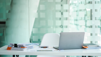 Mockup laptop on desk table with stack of paper and document.