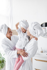 Happy lesbian couple holding daughter in towel and bathrobe in bathroom