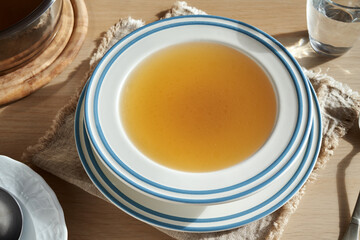 A white and blue soup bowl of beef bone broth on a table in sunlight
