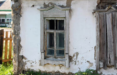 An old, abandoned house with windows in a rustic landscape. A collapsed building with worn paint in a small settlement. Selective focus. Retro and vintage. A copy of the space. Front view. 