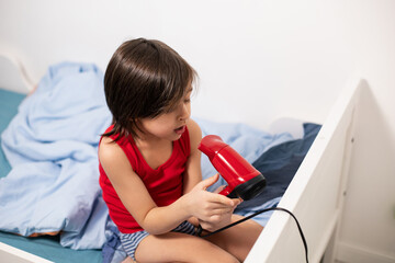 five year old brunette boy with long hair dries his hair with a red hair dryer