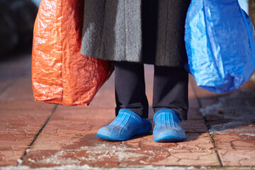 feet of refugees or homeless people in dirty cheap shoes. A faceless woman with large bags in her...