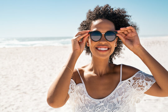 Smiling black woman having fun at beach while wearing sunglasses