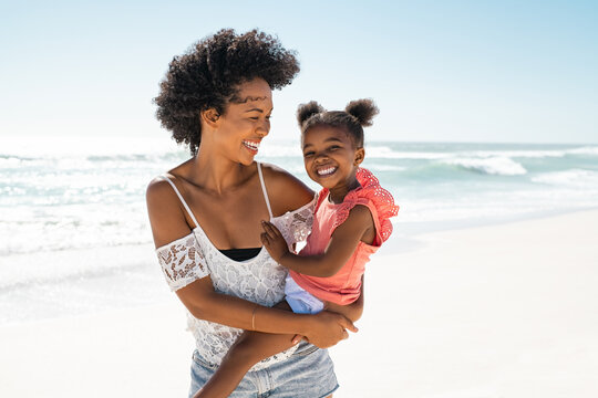 Happy black young mother carrying daughter at beach