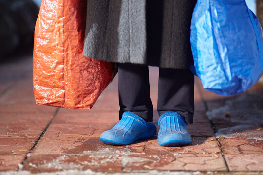 feet of refugees or homeless people in dirty cheap shoes. A faceless woman with large bags in her hands