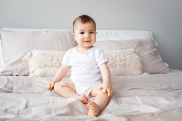 Portrait of a 9-month-old girl with brown eyes sitting on a bed...