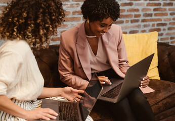 Cheerful multiethnic women working on laptops in office