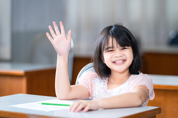 Fototapeta na wymiar A female Asian kid student raising a hand to ask teacher question in the classroom