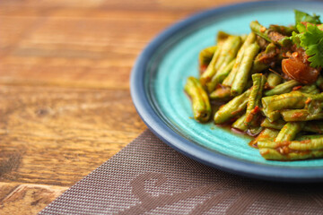 Stir fried pork belly and red curry paste with sting bean served in a blue plate on a wooden table.