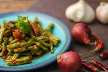 Stir fried pork belly and red curry paste with sting bean served in a blue plate on a wooden table.