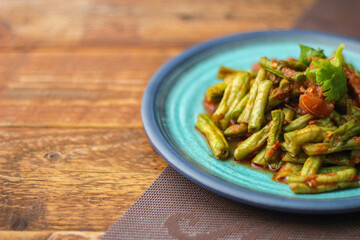 Stir fried pork belly and red curry paste with sting bean served in a blue plate on a wooden table.