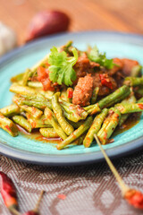 Stir fried pork belly and red curry paste with sting bean served in a blue plate on a wooden table.