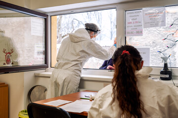 A nurse with shield inserts a swab into a nose to collect a possible positive COVID-19 sample...