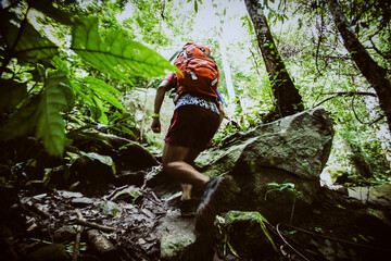 backpack man running up a rocky mountain slope. male trail runner running uphill trekking in...