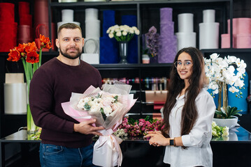 A young bearded man buys a beautiful bouquet of flowers for a girl's holiday in a cozy flower shop. Floristry and bouquet making in a flower shop. Small business.
