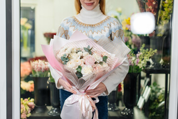 A young girl poses with a beautiful festive bouquet against the background of a cozy flower shop. Floristry and bouquet making in a flower shop. Small business.