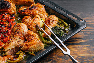 A baking sheet with various portions of fried chicken meat. A set of fried chicken fillet, thigh, wings, strips and legs on the background of the culinary table with spices and cherry tomatoes