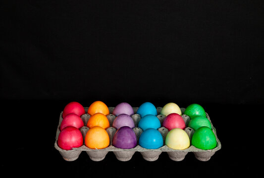 Bright colorful easter eggs in egg box on black background.