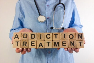 Female doctor holding text addiction treatment from wooden blocks