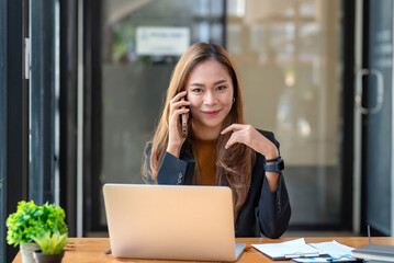 Beautiful smiling young Asian businesswoman at work talking on phone.
