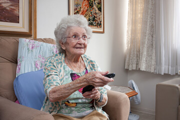 Elderly Lady at home sitting in a chair with a TV Channel Changer in her hand