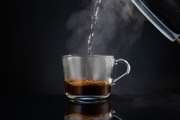 pouring boiling water into coffee in a transparent glass empty mug on a dark background
