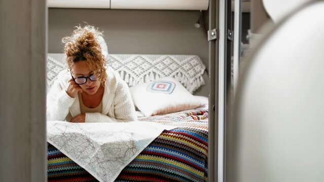 Adult woman laying and relaxin in camper van bedroom using paper guide map to plan next destination. Vaniife and travel people lifestyle concept. Tourist plan activity inside camping car van