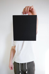 Man holds a black paper box in his hand. Young man with new package. Postal services, delivery. Kraft paper. Gift box, gift. Box close-up. Empty packaging, empty space. Cardboard case 