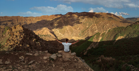 a man sitting on a cliff looking at the mountains ahead during the day in sunny weather