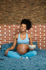 Pregnant woman at home about to eat a healthy salad. Cheerful black expecting mother wearing comfortable clothes.