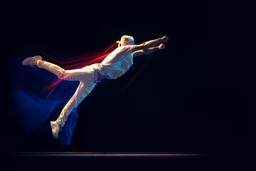 Portrait of man in sports white suit, hip-hop dancer flying isolated on dark background in mixed neon light. Youth culture, hip-hop, movement, style and fashion, action.