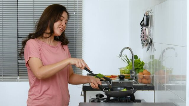 Cheerful young woman dancing while cooking food in the kitchen at home