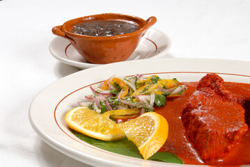 pork dish in adobo with manzano peppers, red onion, orange and beans, mexican food, cochinita pibil