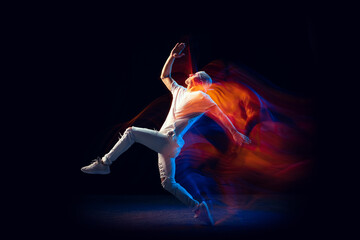 Sportive man in sports white suit dancing hip-hop isolated on dark background in mixed neon light. Youth culture, hip-hop, movement, style and fashion, action.
