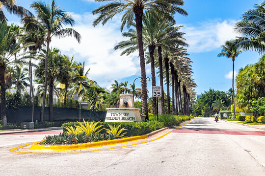 Miami, USA - July 18, 2021: Sign For Welcome To Golden Beach In Miami, Florida With Palm Trees Lining Street Road Collins Avenue On Sunny Day And Blue Sky