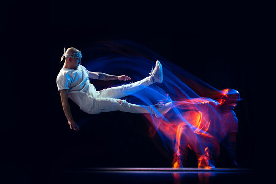 Split personality. Sportive man in sports white uniform and do-rag dancing hip-hop isolated on dark background in mixed neon light. Youth culture, style and fashion
