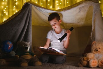Obraz na płótnie Canvas the child is reading a book with a flashlight