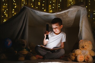 Obraz na płótnie Canvas the child is reading a book with a flashlight