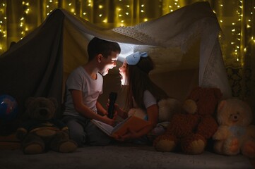 Fototapeta na wymiar children boy and girl playing and frighten each other with flashlight in tent at night