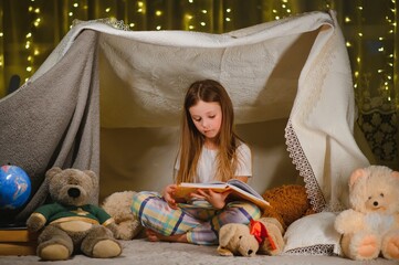 Obraz na płótnie Canvas Reading and family games in children's tent. Little girl with books and flashlight before going to bed.
