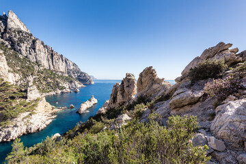 Fototapeta na wymiar Crique de méditerranée étroite aux eaux pures et bleues entourée de falaises calcaires à pic avec un îlot en forme de sous-marin. Calanque de Sugiton, Le Torpilleur.